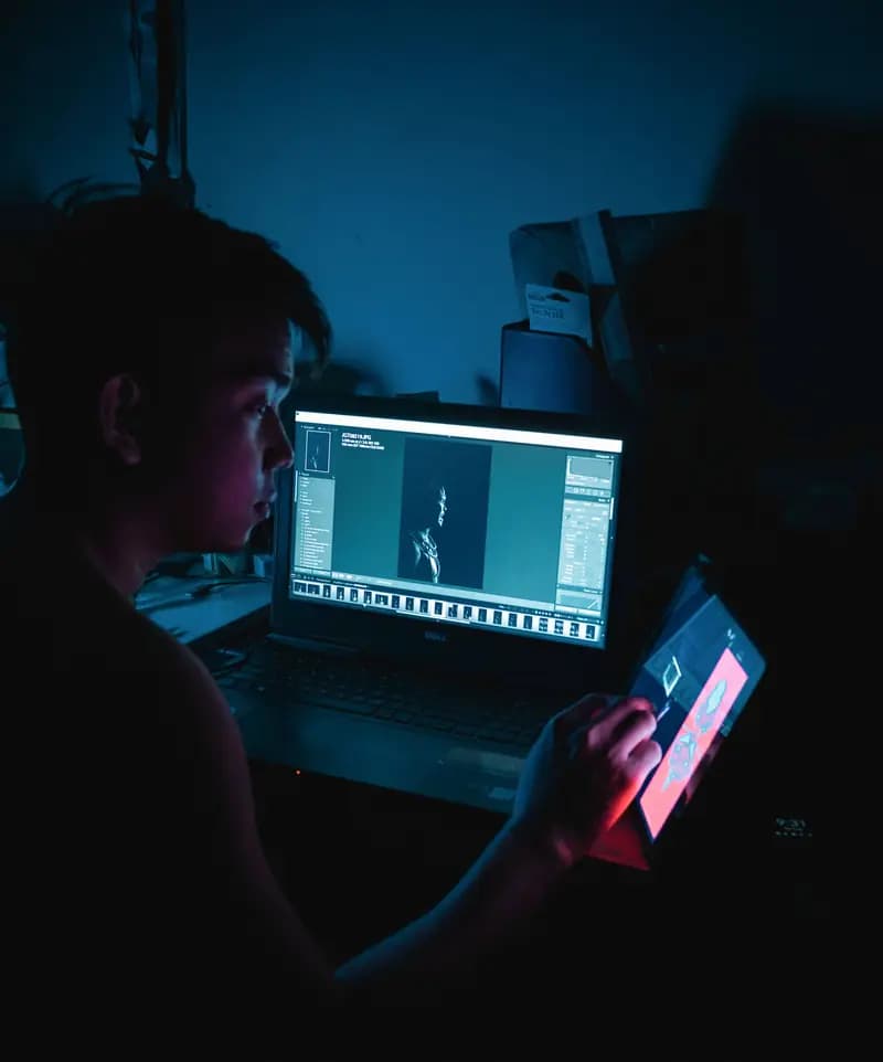Designer working on a laptop and tablet in a dark studio