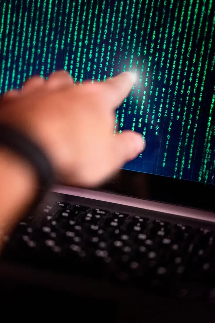 Hand reaching towards a screen of streaming code