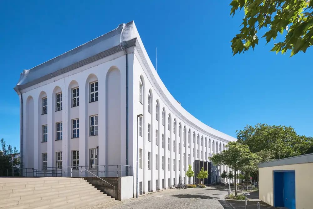 Curved white university building under a blue sky